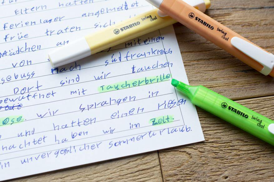 Nahaufnahme eines Aufsatzes eines Grundschülers der vierten Klasse. Einzelne Worte sind mit Textmarkern swing cool von Stabilo markiert.