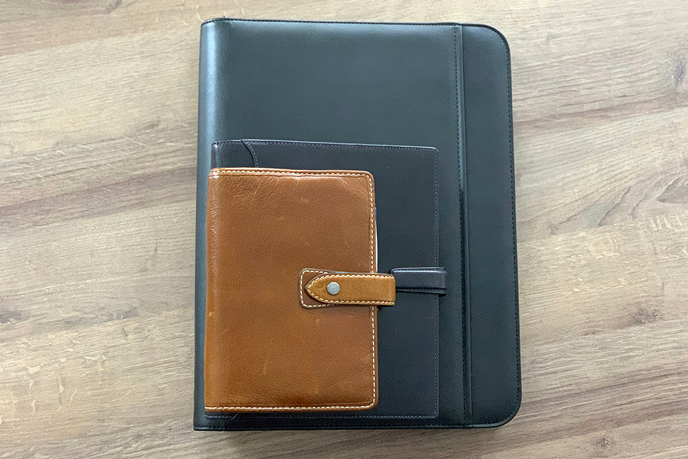 Drei Kalender der Marke Filofax liegen gestapelt auf einem Holztisch.