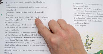 Beim Vorlesen fährt eine Hand mit dem Finger die Zeilen in einem aufgeschlagenen Buch nach. Foto: Johanna Rundel