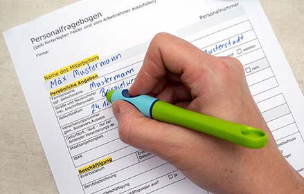 Auf einem grauen Untergrund liegt ein Personalfragebogen-Formular. Eine Hand füllt es mit dem griffix Schreiblern-Tintenroller von Pelikan in Druckbuchstaben aus. Foto: Johanna Rundel
