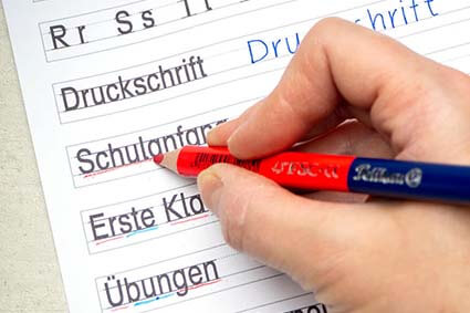 Eine Hand unterstreicht mit einem Silbenstift von Pelikan Druckbuchstaben-Wörter auf einem Schreiblernblatt. Der Stift hat eine rote und eine blaue Spitze. Foto: Johanna Rundel 
