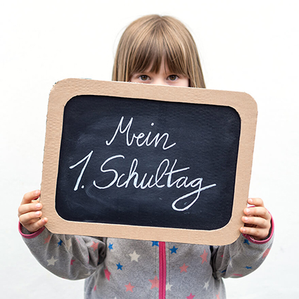 Ein braunhaariges Mädchen im Grundschulalter hält sich eine kleine Schultafel vor das Gesicht, auf der "Mein 1. Schultag" steht. Die verwendete Tafelfolie ist von Knorr-Prandell. Foto: Johanna Rundel