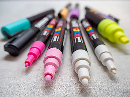 Auf einem hellen Untergrund liegen mehrere Marker der Marke POSCAin unterschiedlichen Farben und mit unterschiedlichen Spitzen. Die Spitzen zeigen Richtung Betrachter und sind im Fokus des Bildes. Foto: Johanna Rundel