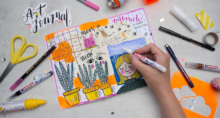 Ein buntes Art Journal Kunstwerk in Mixed-Media Technik mit verschiedenen Papieren, Ausschnitten aus Zeitschriften und Texten - gemalt, geschrieben und schabloniert mit den Produkten von Edding. Es ist eine rosa Katze zu sehen, mehrere Topfpflanzen eine blonde Frau und Augen. Jemand malt gerade ein paar Details mit einem weißen Acrylmarker darauf. Drumherum liegen verschiedene Materialien, die zur Herstellung der Seite benutzt wurden. Foto: Johanna Rundel