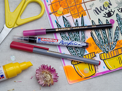 Ein buntes Art Journal Kunstwerk in Mixed-Media Technik mit verschiedenen Papieren, Ausschnitten aus Zeitschriften und Texten. Darauf und daneben liegen eine gelbe Schere und verschiedene Stifte und Marker von Edding, die zur Herstellung verwendet wurden. Foto: Johanna Rundel
