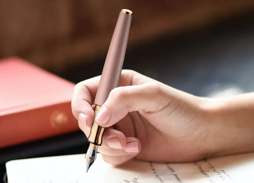 Jemand schreibt mit einem roséfarbenen Füller von Otto Hutt auf ein Blatt Papier.