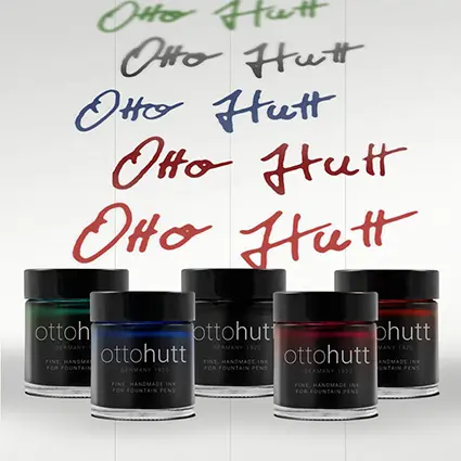 Fünf Tintenfässchen mit verschiedenen Tintenfarben stehen vor einem weißen Hintergrund. Oberhalb wurde in allen Farben der Name Otto Hutt geschrieben.