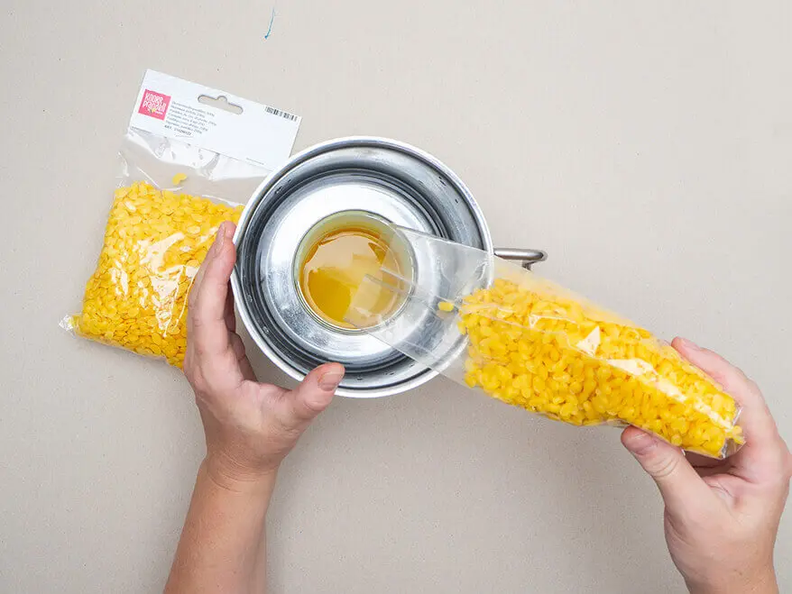 Jemand füllt Bienenwachslinsen von KNORR prandell in eine Blechdose, die in einem Wasserbad im Topf zum Schmelzen steht. Foto: Johanna Rundel