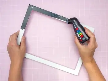 Jemand malt einen weißen Bilderrahmen mit einem breiten Marker von POSCA schwarz an. Foto: Johanna Rundel