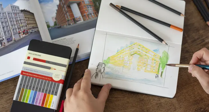 Jemand mal mit Aquarellstiften und Pinsel eine architektonische Zeichnung in ein Skizzenbuch von Moleskine.