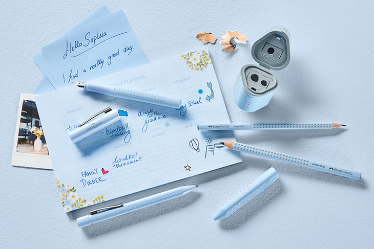 Verschiedene Schreibgeräte in der Grip Sky Blue Edition liegen auf einem Blatt Papier.