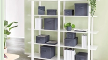 Das Bild zeigt ein weißes Regal mit mehreren dunkelgrauen LEITZ Aufbewahrungsboxen in verschiedenen Größen. Die Boxen sind ordentlich in den Regalfächern platziert und bieten eine funktionale Lösung zur Aufbewahrung von Gegenständen. Einige dekorative Elemente, wie Pflanzen, sind ebenfalls im Regal zu sehen.