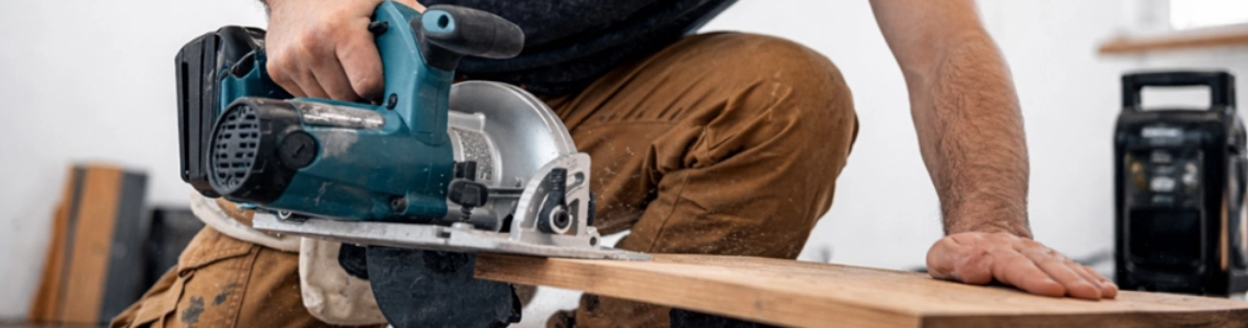 Handwerker mit Schutzbrille schneidet mit Makita Handkreissäge Holzbrett. 