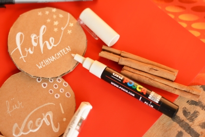 Posca Marker und Zimtstangen neben beschrifteten Anhängern.