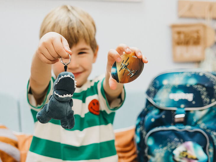 Ein Junge im Grundschulalter hält strahlend einen "Klettie" und einen "Hangie" von ergobag in die Kamera.