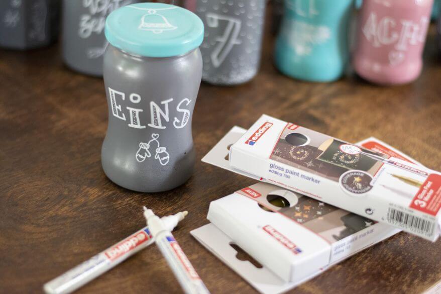 Bemaltes Glas mit „Eins“, daneben Permanentmarker und Verpackungen von Edding.