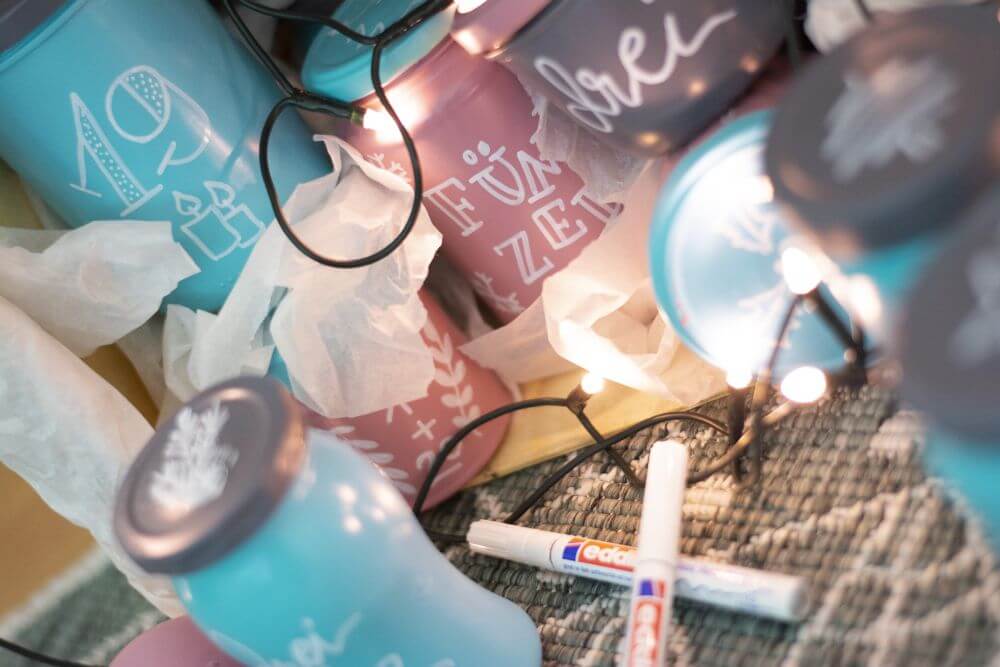 Detailaufnahme eines Upcycling-Adventskalenders aus leeren Marmeladen- und Einmachgläsern: Mit Transparentpapier zwischen den Gläsern wird die Farbe vor Absplittern geschützt.