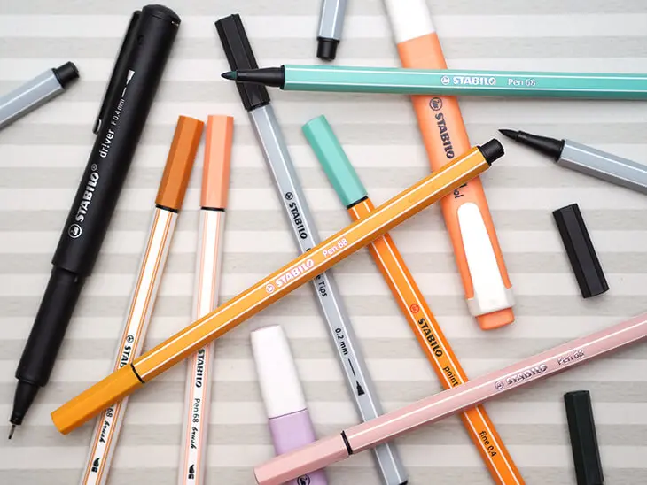 Verschiedene Stifte von STABILO liegen auf einem gestreiften Untergrund. Foto: Johanna Rundel