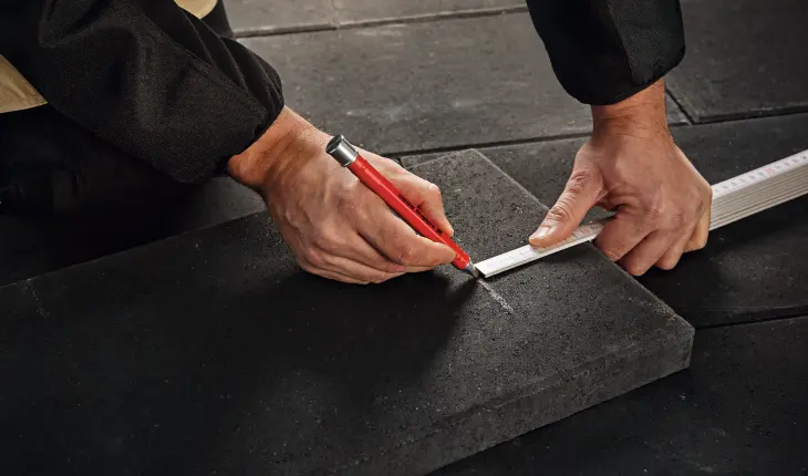 Das Bild zeigt einen Mann, der mit einem edding Zimmermannsbleistift eine Markierung auf einer rauen Steinoberfläche anzeichnet.