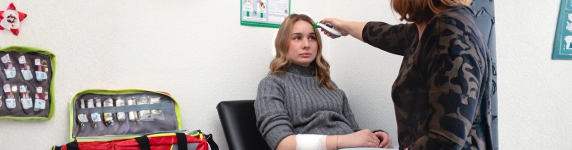 rsthelferin versorgt verletzten Arm einer jungen Frau in einem Erste-Hilfe-Raum.