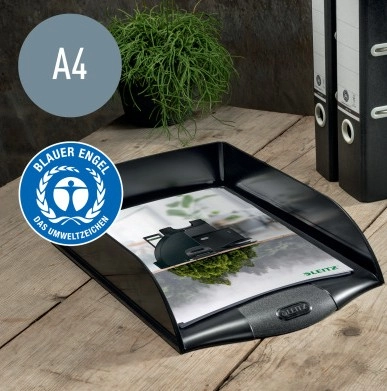 Das Bild zeigt einen schwarzen Leitz Briefkorb im Format A4, der auf einem Holztisch steht. Im Briefkorb liegt ein Dokument, das auf Leitz Büroprodukte verweist. Der Briefkorb ist mit dem Umweltzeichen 'Blauer Engel' ausgezeichnet. Im Hintergrund sind weitere Ordner und eine grüne Pflanze zu sehen.