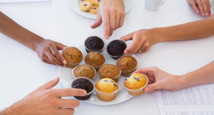 Hände greifen nach Muffins auf einem Konferenztisch