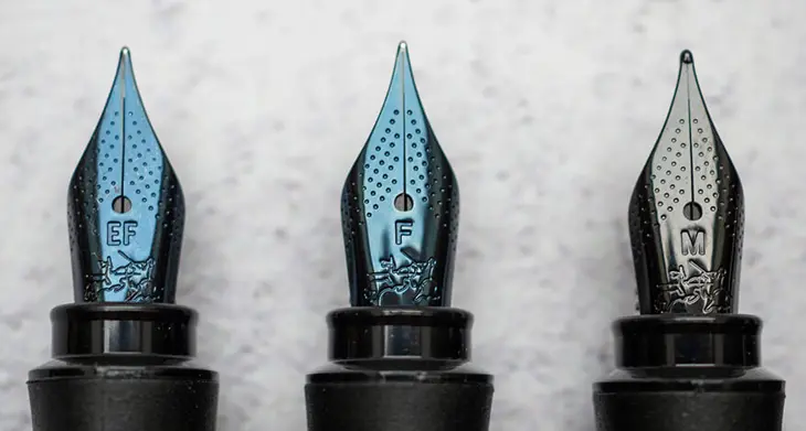 Nahaufnahme dreier Federspitzen von Füllhaltern mit den Abkürzungen EF, F und M.