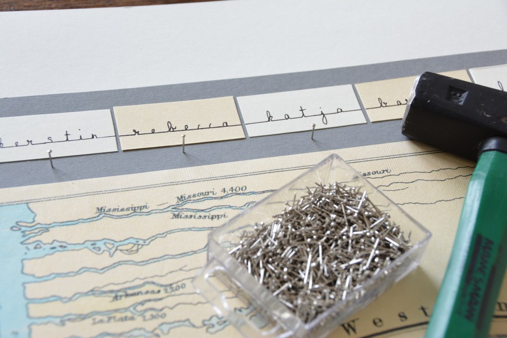 Namensschilder aufgeklebt unterhalb einer Landkarte, kleine Nägel und ein Hammer liegen darauf.