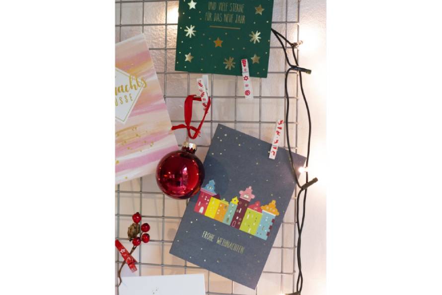 Bunte Weihnachtsarten und roter Kugel an Gitter mit Lichtern befestigt