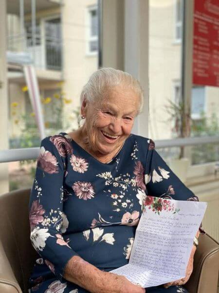 Die Bewohnerin eines Pflegeheims hält lächelnd einen Brief in die Kamera, den sie über die Initiative "Stift und Papier" erhalten hat.