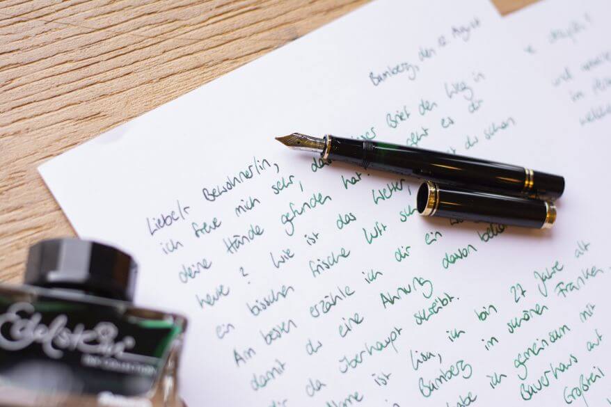 Ein handgeschriebener Brief liegt auf einem Schreibtisch, darauf liegt ein Füllfederhalter "Souverän" und ein Fass Edelsteintinte von Pelikan.