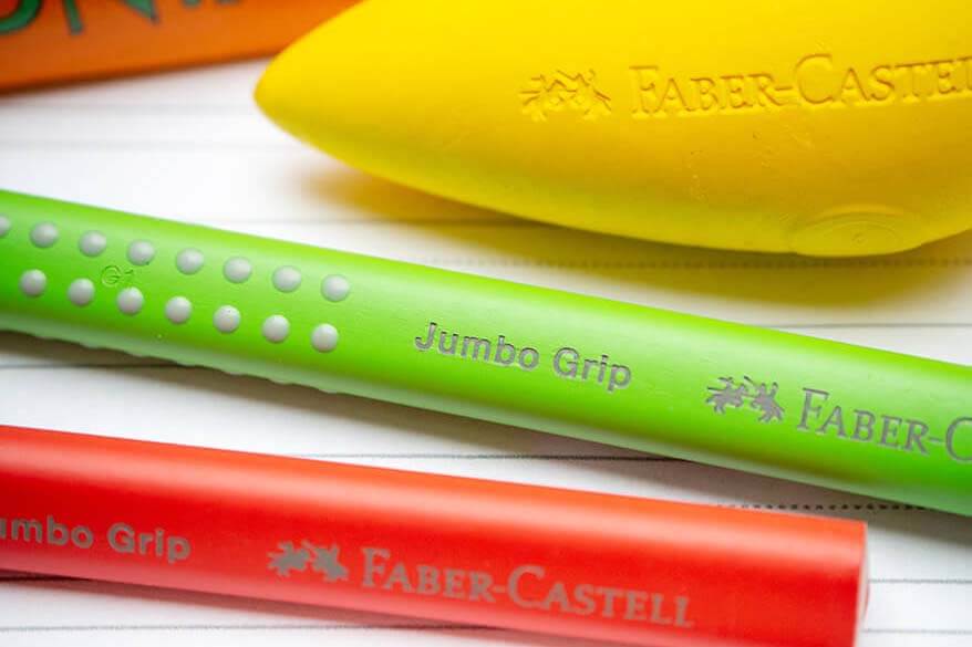 Nahaufnahme verschiedener Stifte der Firma Faber-Castell: Zwei Jumbo Grip Buntstifte in rot und grün sowie eine gelbe, radierbare Malkreide in Birnenform. Foto: Johanna Rundel