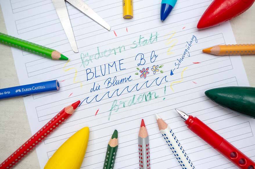 Auf einem Schreiblern-Papier steht ein kurzer Text. Drumherum liegen verschiedene Stifte, Kreiden und eine Schere der Marke Faber-Castell: Scribolino Schreiblernfüller, Scribolino Druckbleistift, Grip Schulschere, Jumbo Grip – wasservermalbare Buntstifte, radierbare Malkreiden „Birne“, Jumbo Grip bicolor, Grip Heft&Tafel. Foto: Johanna Rundel