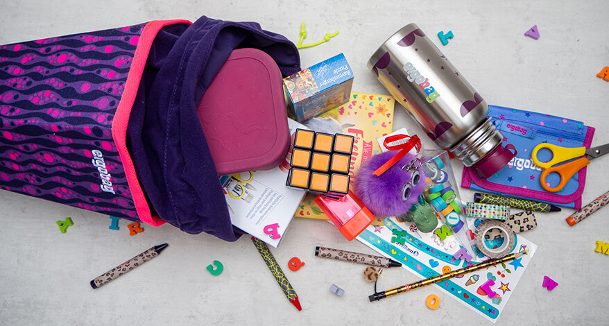 Eine Schultüte der Marke ergobag liegt geöffnet, aus der Schultüte sind verschiedene Teile rausgefallen: Thermoskanne, Schere, Plüschtier, Stifte...