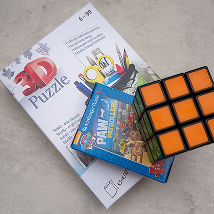 Auf einem hellgrauen Untergrund liegt ein Stapel mit Puzzles. Obendrauf liegt ein gelöster Zauberwürfel. Foto: Johanna Rundel