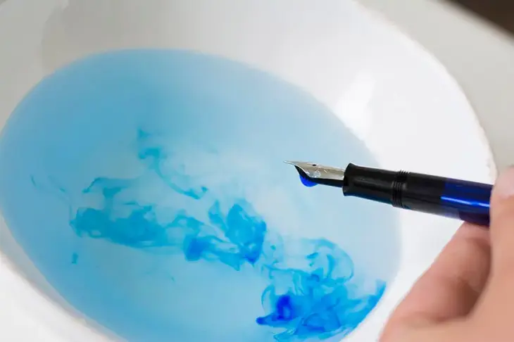 Nahaufnahme der Spitze eines Füllers, die ins Wasser getaucht wurde und an der ein Wassertropfen hängt. 