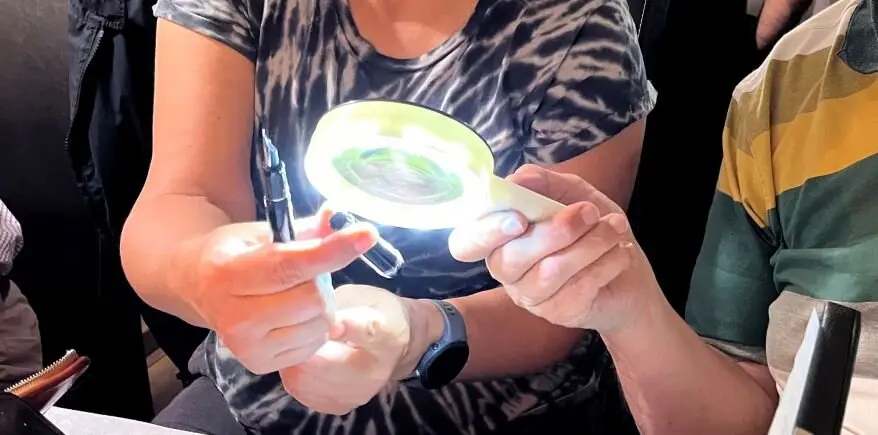 Zwei Menschen betrachten einen Füller durch eine Lupe mit integrierter Beleuchtung.