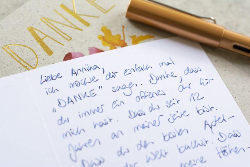 Detailaufnahme einer Dankeskarte mit handgeschriebenem Text. Daneben liegt ein Füllhalter.