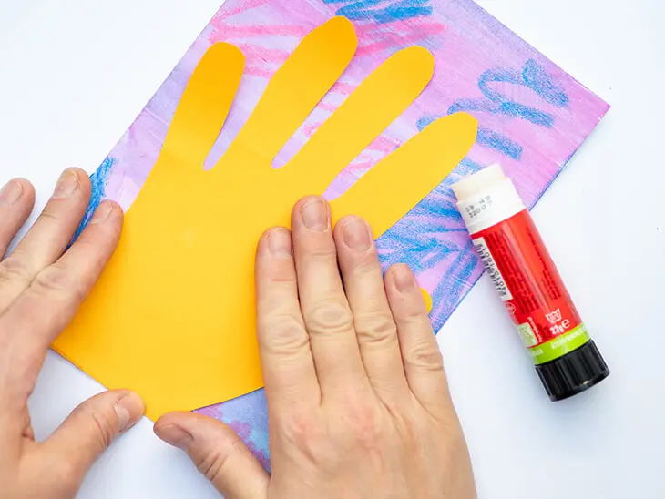 Jemand klebt eine aus Tonpapier ausgeschnittene Hand auf einen mit Farben von STAEDTLER bemalten Karton. Foto: Johanna Rundell