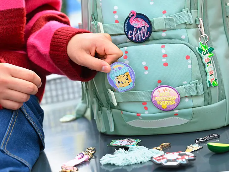 Jemand heftet ein Patch an einen Schulrucksack von coocazoo.