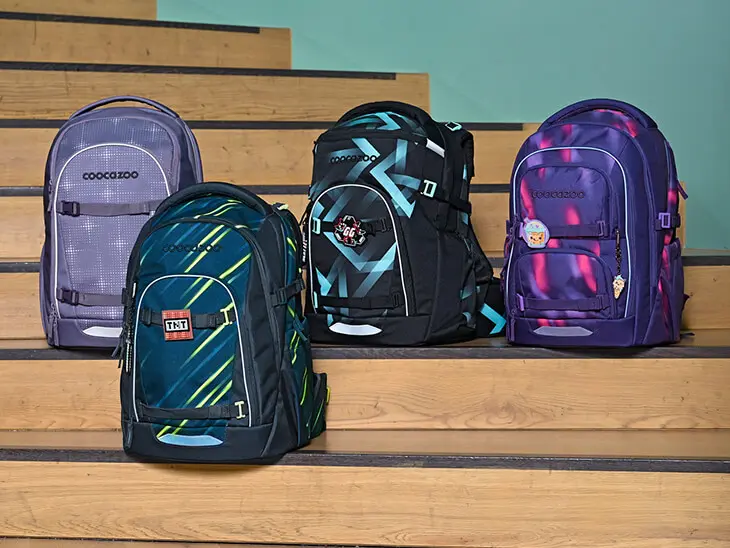 Vier verschiedene Schulrucksäcke von coocazoo stehen nebeneinander auf einer Treppe.