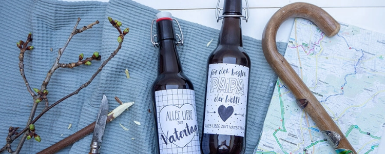 2 Bierflaschen mit selbst gestaltetem Etikett, Wanderstock, Wanderkarte liegen auf einem Tisch