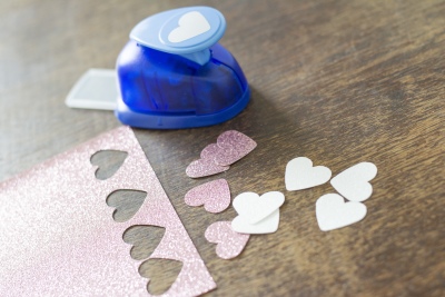 Herzstanzer und Glitzerpapier mit ausgestanzten Herzen in Rosa und Weiß