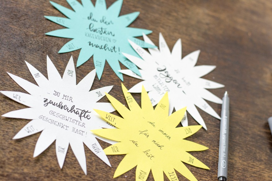 Farbige Papierblumen mit handgeschriebenen Botschaften auf Holztisch
