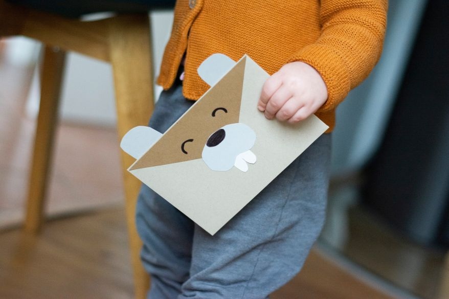 Kind hält Einladungskarte zum Kindergeburtstag in der Hand. Selbst gebastelte Do it yourself-Karte als Biber.