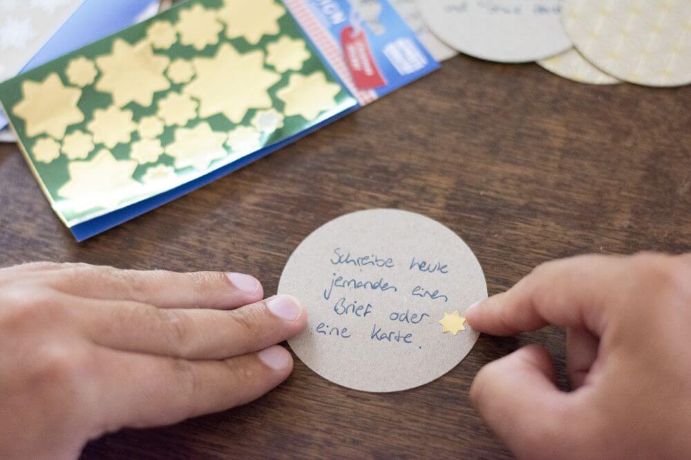 Ein mit Tinte beschriebener Motivkarton wird mit einem goldenen Sticker in Sternform von Avery Zweckform beklebt.