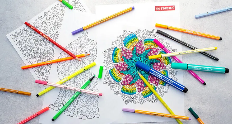 Auf einem grauen Untergrund liegen mehrere Mandalas zum Ausdrucken. Verschiedene Stifte von Stabilo sind im Bild verteilt.