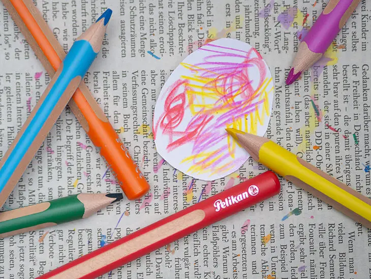 Auf Zeitungspapier liegen bunte griffix-Buntstifte von Pelikan und ein bekritzeltes, weißes Ei aus Papier. Foto: Johanna Rundel
