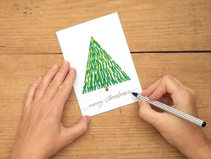 Jemand schreibt mit einem Fineliner von edding "Merry Christmas" auf eine Karte. Foto: Johanna Rundel