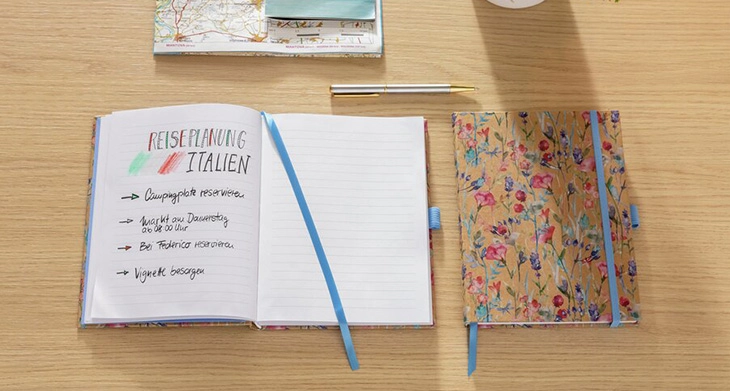 Florales Notizbuch mit Reiseplanung und Karte auf Schreibtisch.